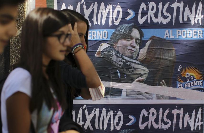 Jóvenes caminan frente a una pared con carteles alusivos a Máximo Kirchner, hijo de la mandataria argentina, Cristina Fernández. (EFE) 