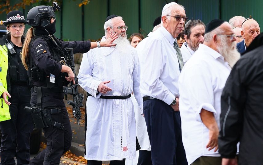 El rabino Daniel Walker (3.a izq.) se encuentra entre agentes de policía armados mientras conversan con miembros de la comunidad judía frente a la sinagoga de la Congregación Hebrea de Heaton Park en Crumpsall, al norte de Manchester, el 2 de octubre de 2025, tras un ataque en la sinagoga.&nbsp; &nbsp;&nbsp;