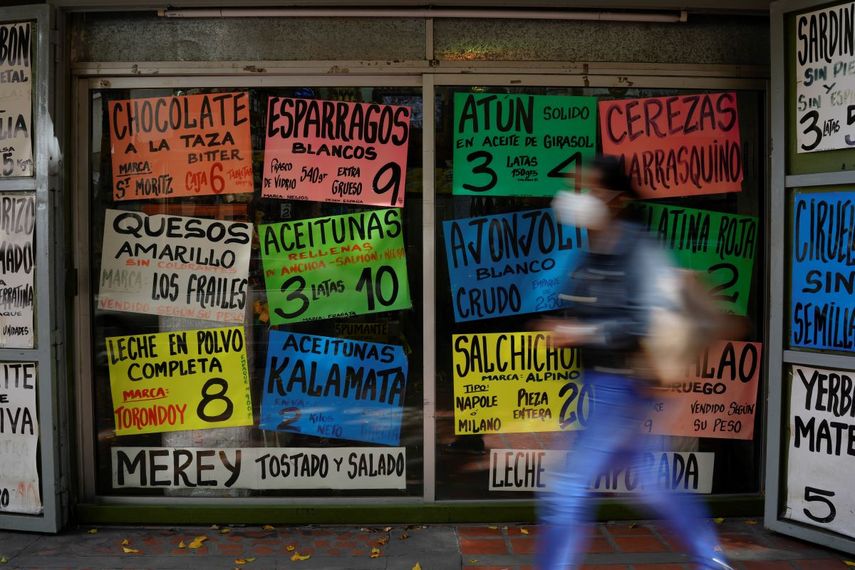 Una mujer camina frente a carteles que muestran los precios de los productos en dólares estadounidenses, frente a una tienda de comestibles en Caracas, Venezuela, el martes 18 de enero de 2022.