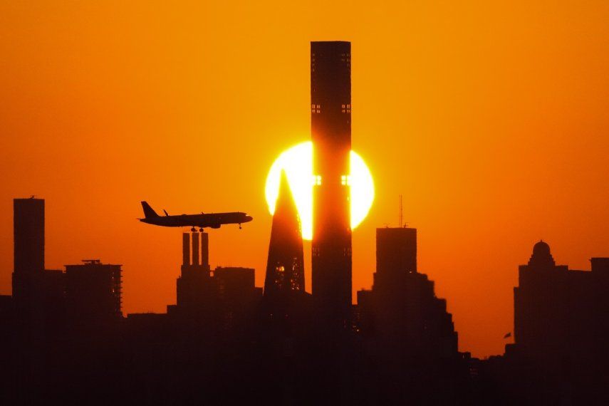 ARCHIVO- Se pone el sol detrás de los rascacielos de Nueva York y un avión se aproxima al Aeropuerto LaGuardia, 6 de setiembre de 2023, en Nueva York. Comienzan los viajes de vacaciones en autopistas, trenes y aviones en Estados Unidos.&nbsp;