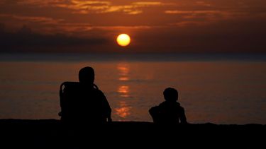 Dos personas observan el ocaso en Surfside, Florida. Para desconcierto de los meteorólogos, no ha habido un solo huracán en el Atlántico desde principios de julio hasta fines de agosto del 2022.