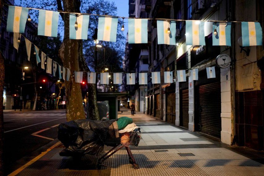 Una persona sin hogar duerme en una cama improvisada montada con un carro de la compra y un banco de la calle, en una zona decorada con banderas de Argentina, en Buenos Aires, Argentina