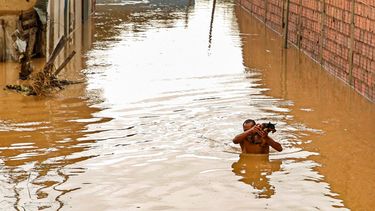 Un hombre carga a su perro en una calle inundada en Itapetinga, estado de Bahia, Brasil, el lunes 27 de diciembre de 2021.