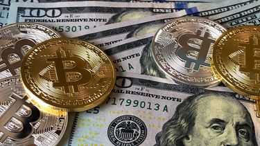 Monedas de bitcoin sogre billetes de 100 dólares estadounidenses.