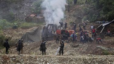 Mineros de oro intentan apagar un incendio en una maquinaria mientras soldados montan guardia cerca como parte de una operación de las Fuerzas Armadas colombianas contra la minera de oro ilegal en Magüi Payán, Colombia, el martes. 20 de abril de 2021