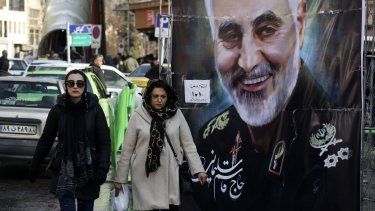 Mujeres caminan junto a un cartel con la imagen del general Qassem Soleimani.
