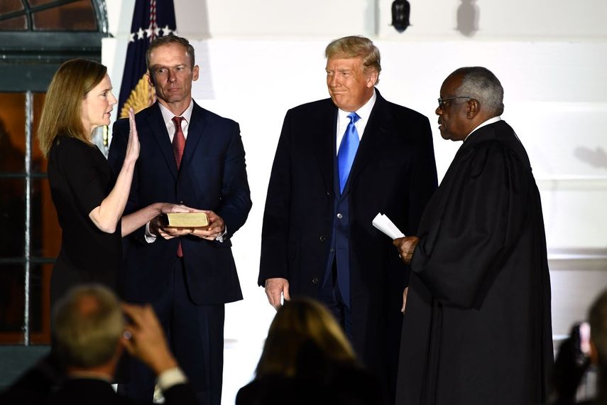 El presidente Donald Trump observa cómo el magistrado de la Corte Suprema, Clarence Thomas (derecha), jura a la jueza Amy Coney Barrett como juez de la Corte Suprema de Estados Unidos, flanqueada por su esposo Jesse M. Barrett, durante una ceremonia en el jardín sur de la Casa Blanca el 26 de octubre de 2020 en Washington, DC.&nbsp;