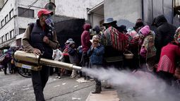 Un trabajador rocía desinfectante alrededor de las personas que viajaron desde las provincias a la iglesia Monte de Oración para comprar alimentos y ropa durante la campaña anual del Buen Samaritano de la iglesia en La Paz, Bolivia, el martes 28 de diciembre de 2021. Debido a la pandemia de COVID-19, la iglesia está distribuyendo la mercadería al aire libre.
