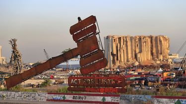 Un mazo monumental, símbolo de la justicia, se alza frente a los restos de silos destruidos por la gran explosión de agosto de 2020 en el puerto que causó más de 200 muertes en Beirut, Líbano, miércoles 4 de agosto de 2021.&nbsp; 