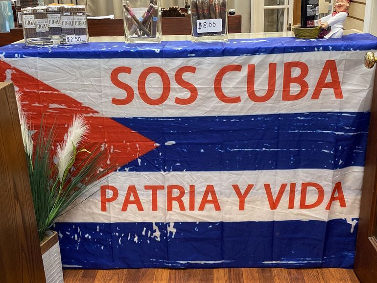 En un mostrador en un shop de tabacos, en el casco histórico de San Agustín, han desplegado una bandera cubana con la emblemática frase de la canción Patria y Vida, con la que un grupo de artistas iniciaron un movimiento a favor de la democracia en Cuba. 