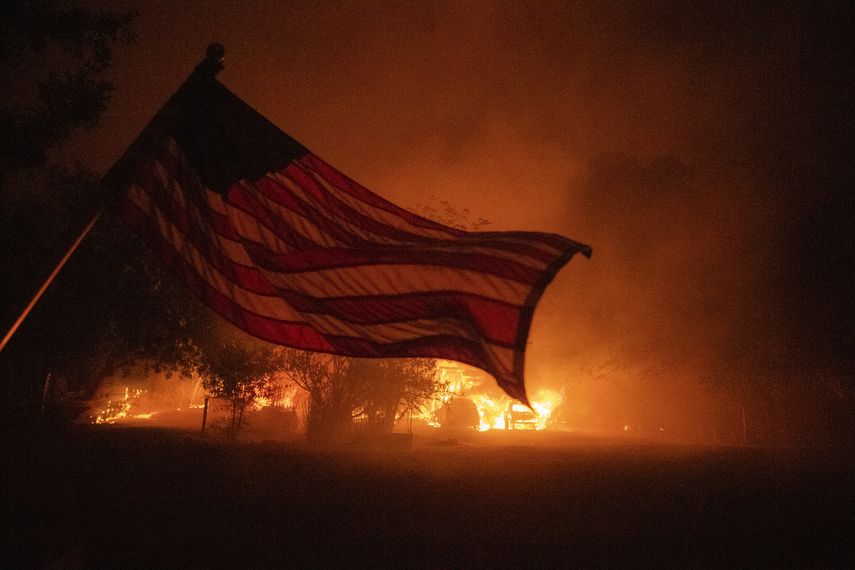 Una bandera estadounidense ondea en el viento frente a una casa en llamas en Vacaville, California, durante el incendio del Complejo Rel&aacute;mpago LNU el 19 de agosto de 2020.&nbsp;