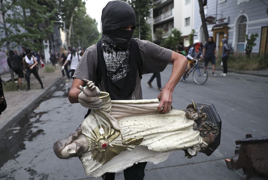 Un manifestante enmascarado remueve una estatua de Jesucristo de una iglesia para usarla en una barricada en Santiago de Chile el viernes 8 de noviembre de 2019.