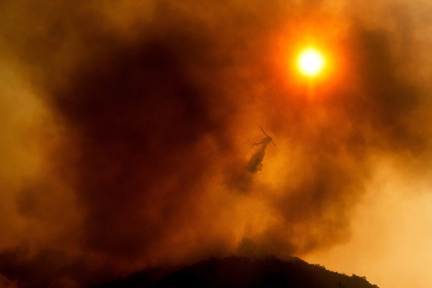 En esta fotografía del lunes 17 de agosto de 2020 un helicóptero arroja agua mientras combate un incendio forestal en Salinas, California