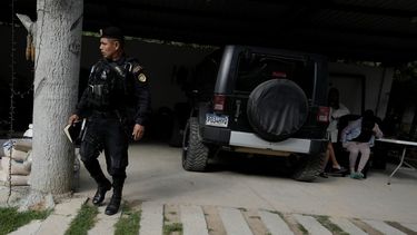 Un policía guatemalteco camina cerca de presuntos traficantes de migrantes, a la derecha, quienes fueron detenidos durante una operación contra una supuesta red de coyotes en Huehuetenango, Guatemala, cerca de la frontera con México, el martes 2 de agosto de 2022