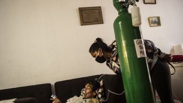 La hija de German Blanco, de 30 años, revisa a su padre mientras está acostado en un sofá en la sala de estar conectada a un tanque de oxígeno en su casa en Callao, Perú, el 4 de febrero de 2021. En Perú, con una población de 33 millones y más de 1,14 millones de personas infectadas, las muertes diarias se duplicaron a más de un centenar a finales de enero. Desde mayo, el país enfrenta una escasez de oxígeno médico que ha llevado a cientos de habitantes a hacer cola hasta 72 horas, durmiendo en las calles, para comprar este gas que el gobierno ha declarado recurso estratégico.