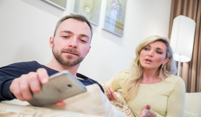 Un hombre mira a su teléfono mientras una mujer le habla. 