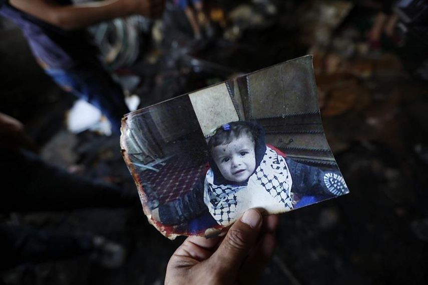 Un familiar muestra una fotografía del bebé palestino de 18 meses Ali Dawabsha, que murió en su casa en un incendio provocado por colonos extremistas israelíes. (EFE)