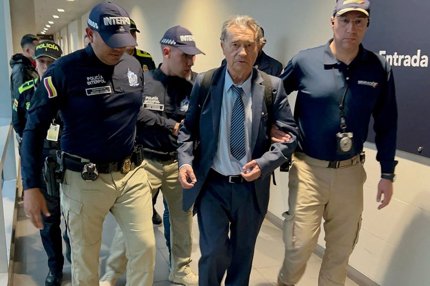 Esta fotografía difundida por la Oficina de Migración de Colombia muestra a agentes de migración y policías colombianos escoltando al ex capo del Cártel de Medellín Carlos Lehder Rivas (C) durante su llegada tras ser deportado de Frankfurt al Aeropuerto Internacional El Dorado de Bogotá el 28 de marzo de 2025.