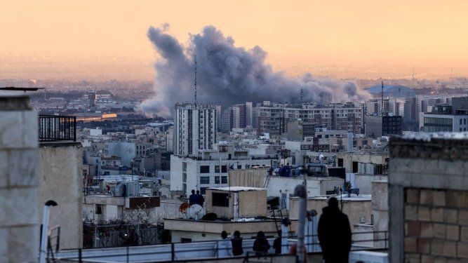 En Irán, una persona observa desde la azotea de un edificio una columna de humo tras un ataque a Teherán, el 3 de marzo de 2026.