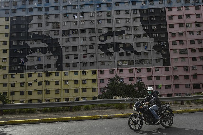Un motorista, con mascarilla para protegerse del coronavirus, pasa por delante del mural Los ojos de Ch&aacute;vez, un dise&ntilde;o basado en los ojos del fallecido expresidente venezolano Hugo Ch&aacute;vez, en el vecindario 23 de Enero, en Caracas, Venezuela, el 30 de julio de 2020.&nbsp;