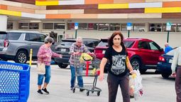 Personas saliendo del mercado, con el área de parqueo al fondo Personas saliendo del mercado, con el área de parqueo al fondo