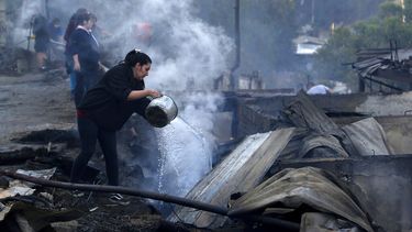 Residentes arrojan agua sobre los restos de sus casas despu&eacute;s que un incendio da&ntilde;&oacute; decenas de viviendas en las afueras de Valpara&iacute;so.