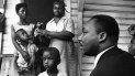 El Dr. Martin Luther King Jr., a la derecha, conversa con afroamericanos de Greenwood, Mississippi, en el porche de su casa el 21 de julio de 1964, durante su campaña puerta a puerta, diciéndoles que se registren para votar y apoyen a su partido Demócrata por la Libertad de Mississippi.