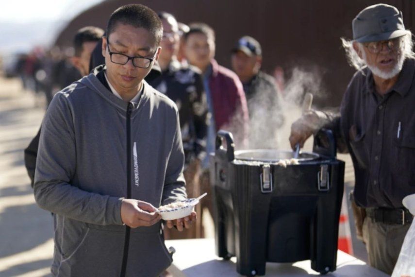 Un chino recibe avena cocida de manos de un voluntario mientras aguarda junto con otras personas a solicitar asilo tras cruzar la frontera con México, el martes 24 de octubre de 2023, cerca de Jacumba, California.