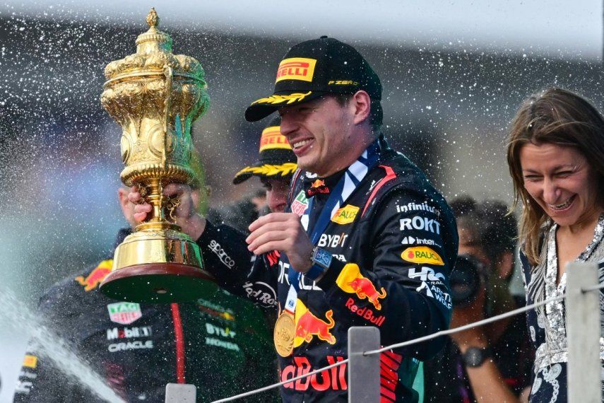 El piloto holandés de Red Bull Racing, Max Verstappen, que sostiene el trofeo, reacciona cuando el segundo clasificado, el piloto británico de McLaren, Lando Norris, rocía champán durante la ceremonia del podio del Gran Premio de Gran Bretaña de Fórmula Uno en el circuito de carreras de Silverstone, en el centro de Inglaterra, el 9 de julio de 2023. &nbsp;