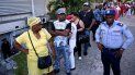 Cubanos hacen fila, bajo la custodia de un agente del régimen. 
