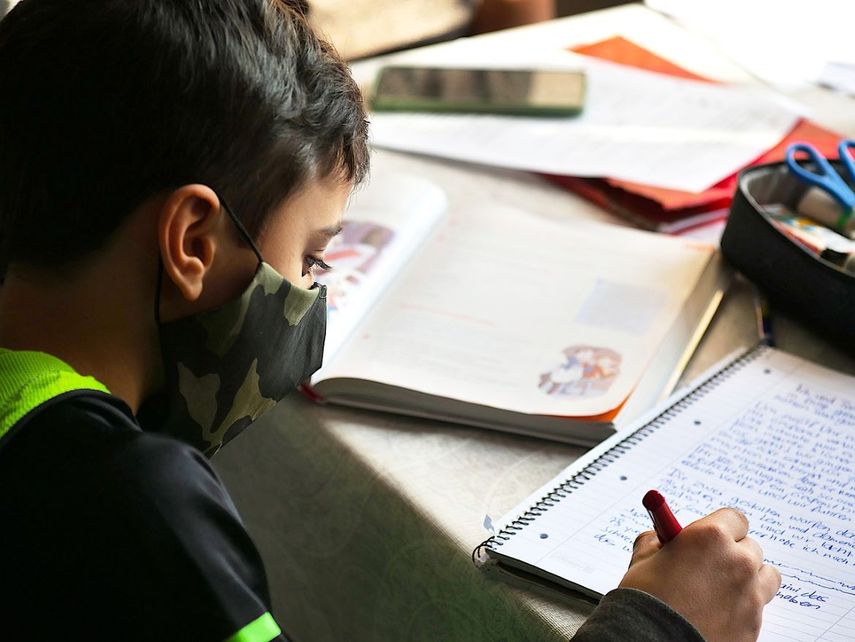 Un niño realiza sus tareas escolares mientras usa una mascarilla contra el COVID-19.