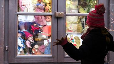 Niña observa juguetes en una tienda a través de una ventana.