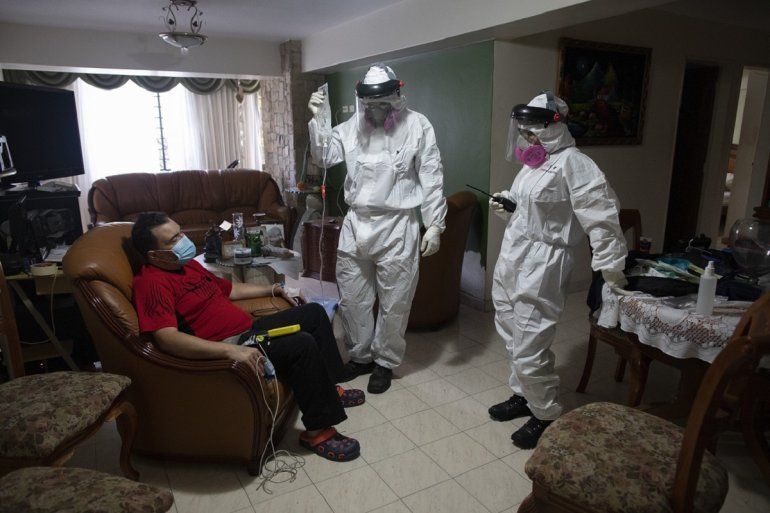 La socorrista voluntaria Zuli Rodiz (der) y el doctor Brayan Alfaro (centro) asisten en su casa a un individuo que se sospecha contrajo el coronavirus el 11 de febrero del 2021 en Caracas.