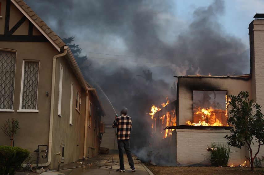 Una persona usa una manguera de jardín para intentar evitar que una casa vecina se incendie durante el incendio de Eaton el 8 de enero de 2025 en Altadena, California.