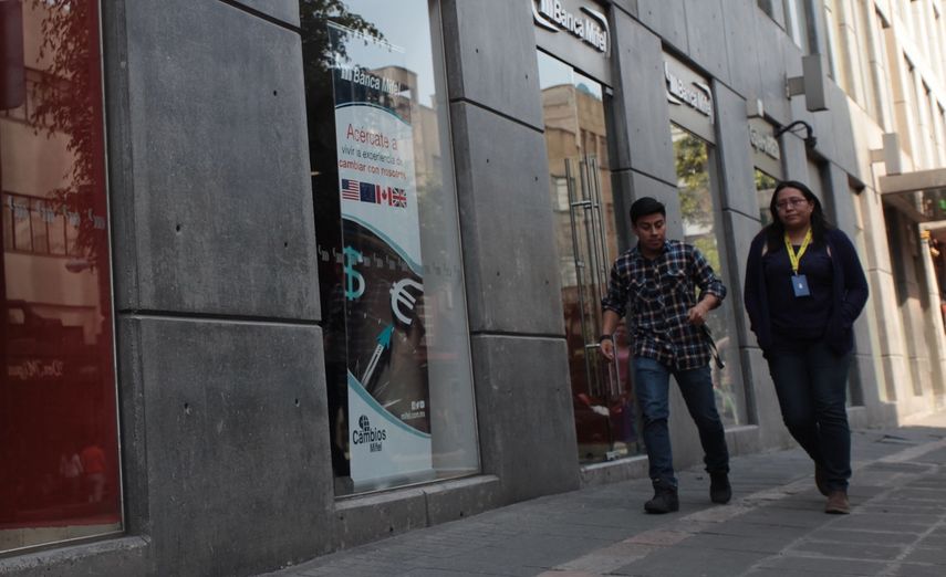 Dos personas caminan frente a la sede de un banco en Ciudad de México.