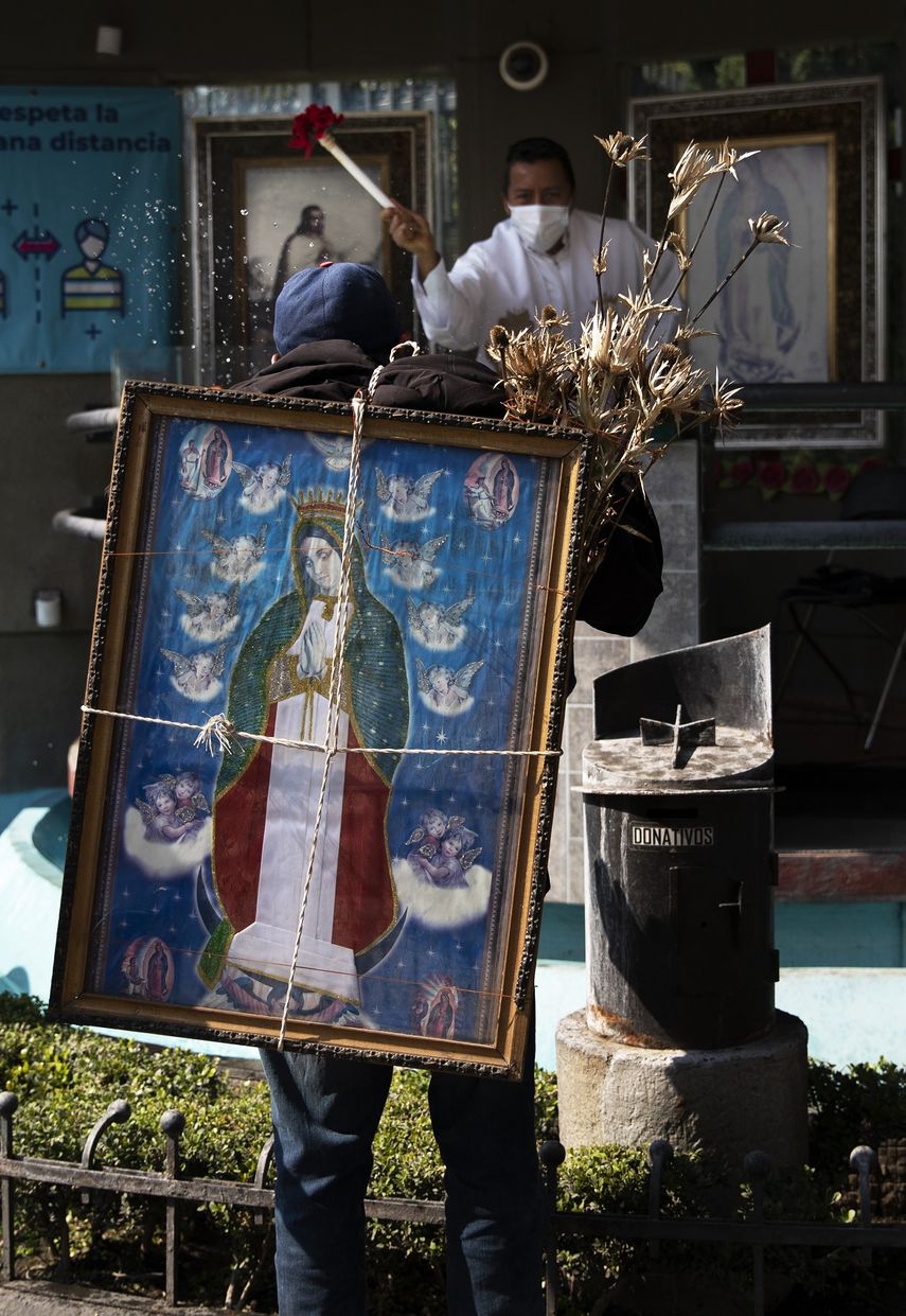 Alejandro Castillo González es rociado con agua bendita por un sacerdote mientras carga una imagen de la Virgen de Guadalupe en su espalda, afuera de la Basílica de la Virgen de Guadalupe en la Ciudad de México, el miércoles 9 de diciembre de 2020.
