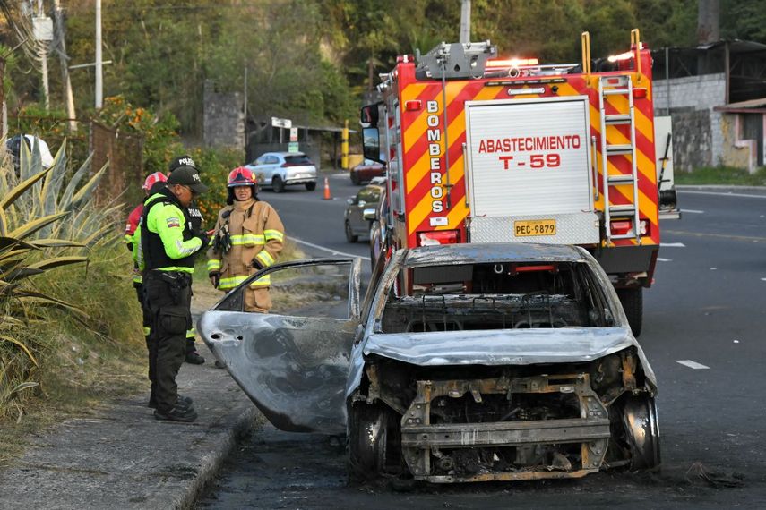 Policías y bomberos permanecen junto a un vehículo calcinado —que presuntamente transportó a los responsables de colocar una bomba— en las afueras de Quito, el 29 de junio de 2026.