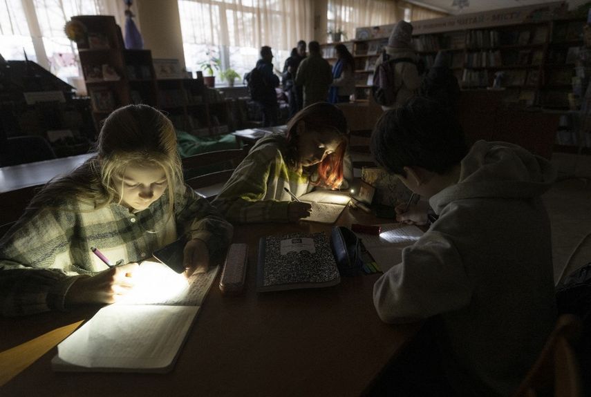 Los niños usan linternas mientras asisten a una reunión de su club de literatura en una biblioteca pública durante un corte de energía en Irpin, al noroeste de Kyiv, el 23 de diciembre de 2022, en medio de la invasión rusa de Ucrania.