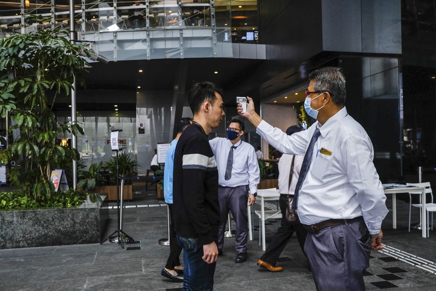 En esta imagen, tomada el 16 de marzo de 2020, un hombre toma la temperatura a una visitante antes de entrar a la Plaza Asia Tower en Singapur.&nbsp;