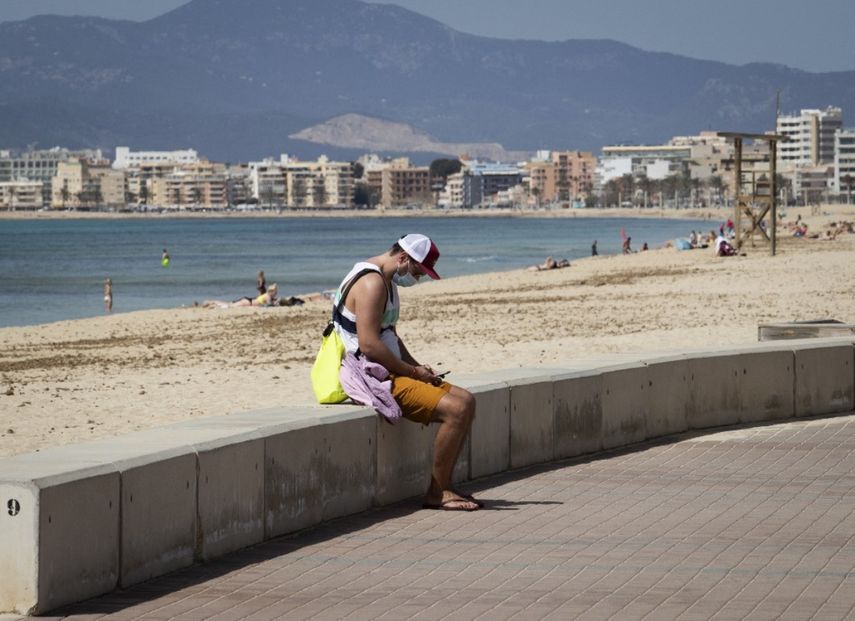 Un turista mira su teléfono en la playa de Palma en Palma de Mallorca el 29 de marzo de 2021. Las reservas para las Baleares aumentaron después de que Berlín a mediados de marzo dejó de exigir a las personas que regresaban de la región a la cuarentena debido a la baja tasa de infección en el archipiélago, que ha sido durante mucho tiempo popular entre los alemanes.