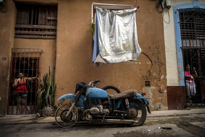 Mujeres miran desde sus puertas delanteras hacia una calle donde una motocicleta con sidecar está estacionada fuera de uso debido a la falta de repuestos, en La Habana, Cuba, el sábado 7 de noviembre de 2020.&nbsp;