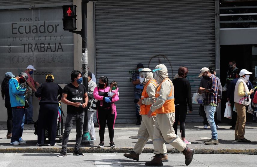Trabajadores con trajes de protección para prevenir el nuevo coronavirus caminan junto a peatones en Quito, Ecuador, el miércoles 10 de junio de 2020.&nbsp;