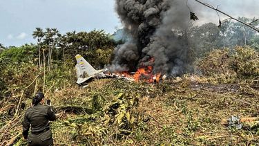 Llamas y una espesa columna de humo negro se elevan desde un avión Hércules de la Fuerza Aérea que se estrelló durante el despegue, mientras un miembro de la Policía colombiana permanece cerca, en Puerto Leguizamo, Colombia, cerca de la frontera sur con Ecuador, el 23 de marzo de 2026.