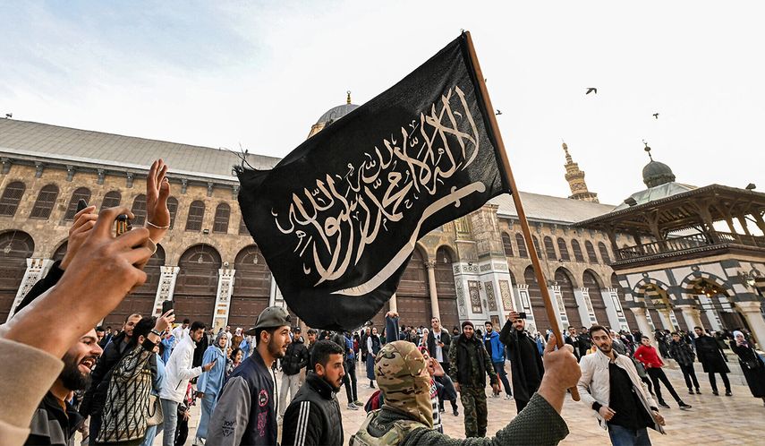 Un combatiente rebelde sirio sostiene una bandera negra islamista que representa lealtad al culto musulmán, mientras camina por el patio de la Gran Mezquita de Damasco del siglo VIII.