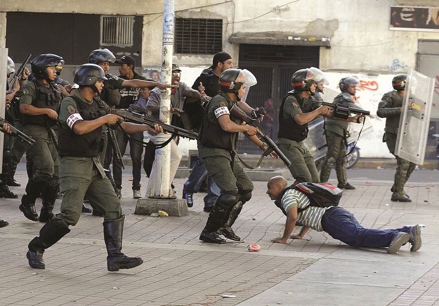 Uniformados de la Guardia Nacional venezolana apuntan sus armas a un ciudadano en la calle.