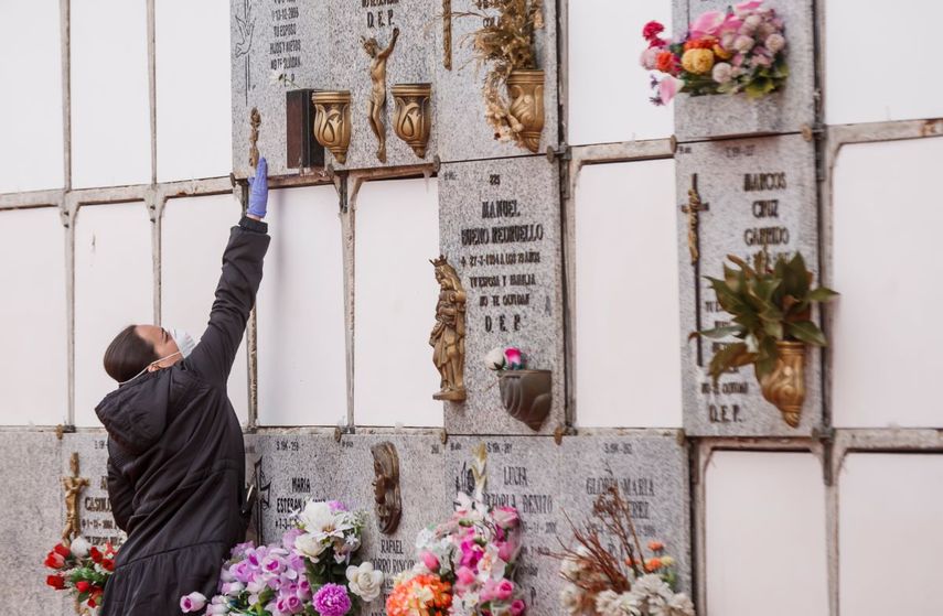 Una mujer que usa una máscara facial y guantes toca la última morada de un hombre que murió por el nuevo coronavirus y que fue enterrado en el cementerio municipal del sur de Madrid, el 23 de marzo de 2020. 