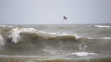 Olas impulsadas por los vientos de Dorian rompen frente a un embarcadero en Vero Beach, Florida, donde alguien plantó una bandera de EEUU.