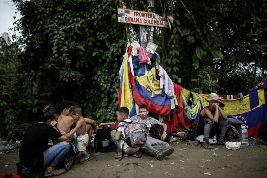 Migrantes sentados bajo un cartel que marca la frontera entre Colombia y Panamá durante su travesía a través del Tapón del Darién, el 9 de mayo de 2023. Cientos de personas que han cruzado la selva han sufridos robos y otros abusos, incluyendo violencia sexual.