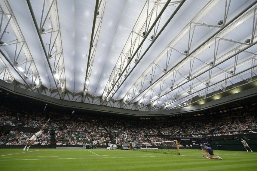 El serbio Novak Djokovic (izq.) le sirve al francés Alexandre Muller bajo el techo cerrado de la cancha central de tenis durante su partido de primera ronda de individuales masculino en el segundo día del Campeonato de Wimbledon 2025 en el All England Lawn Tennis and Croquet Club en Wimbledon, al suroeste de Londres, el 1 de julio de 2025.