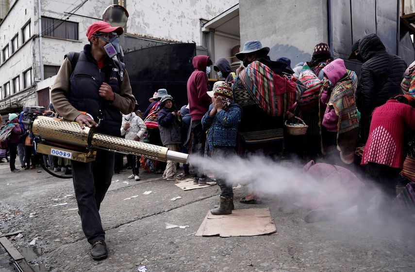 Un trabajador rocía desinfectante alrededor de las personas que viajaron desde las provincias a la iglesia Monte de Oración para comprar alimentos y ropa durante la campaña anual del Buen Samaritano de la iglesia en La Paz, Bolivia, el martes 28 de diciembre de 2021. Debido a la pandemia de COVID-19, la iglesia está distribuyendo la mercadería al aire libre.